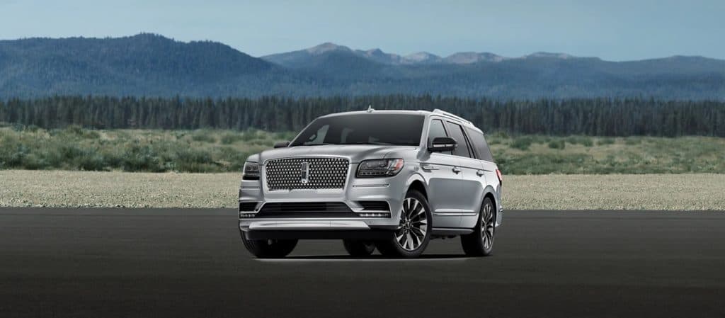 Silver SUV parked on a road with scenic mountain and forest backdrop under a clear sky.