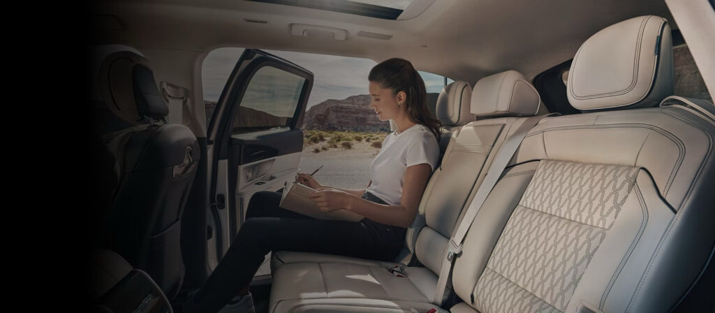 Woman writing in a notebook in the back seat of a luxury SUV with scenic desert view.