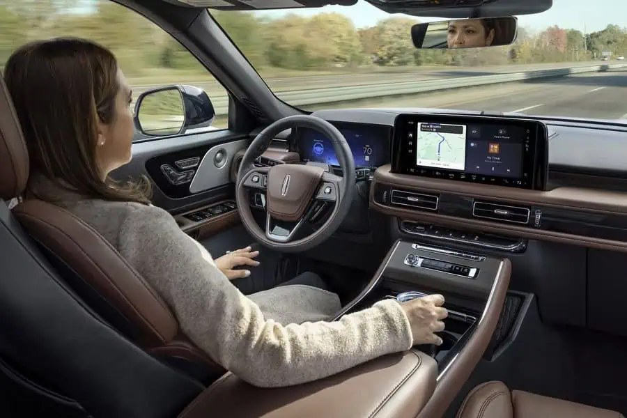 Woman driving a car with a digital dashboard and navigation system on highway.