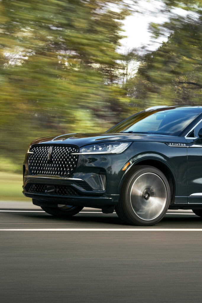 Sleek black SUV driving on a road, blurred trees in the background indicate motion.