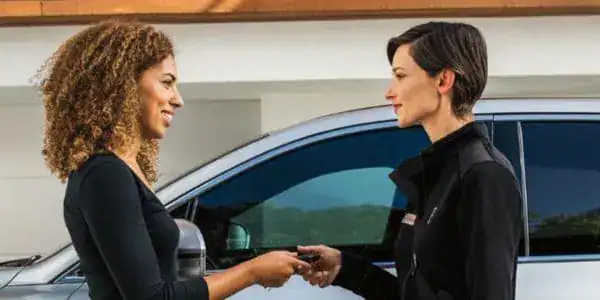 Two women exchanging car keys, standing by a vehicle.