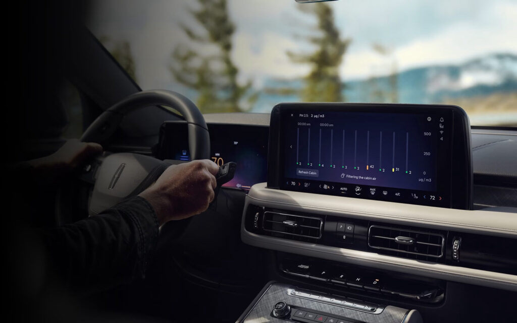 Car dashboard with digital display showing cabin air filtration data, steering wheel, and controls.