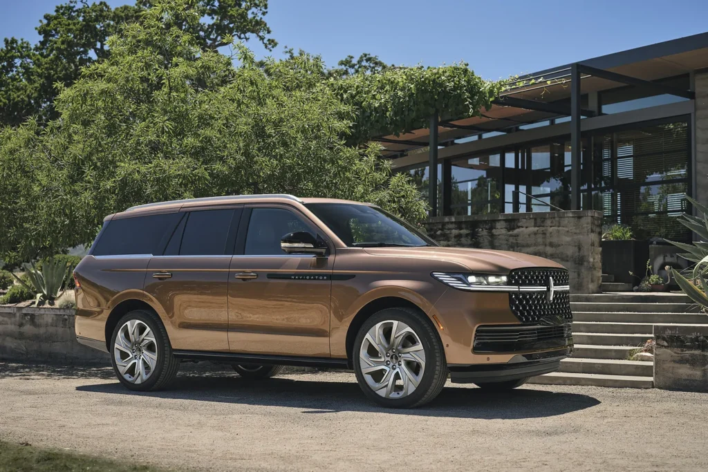 Luxurious brown SUV parked in front of a modern house with lush greenery.