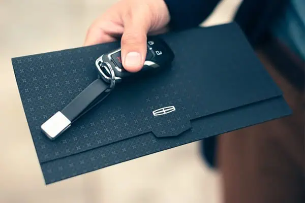 Hand holding a luxury car key and stylish black envelope, symbolizing elegance and high-end vehicles.